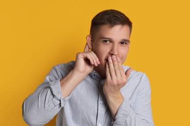 Photo of Man showing hand to ear gesture on orange background