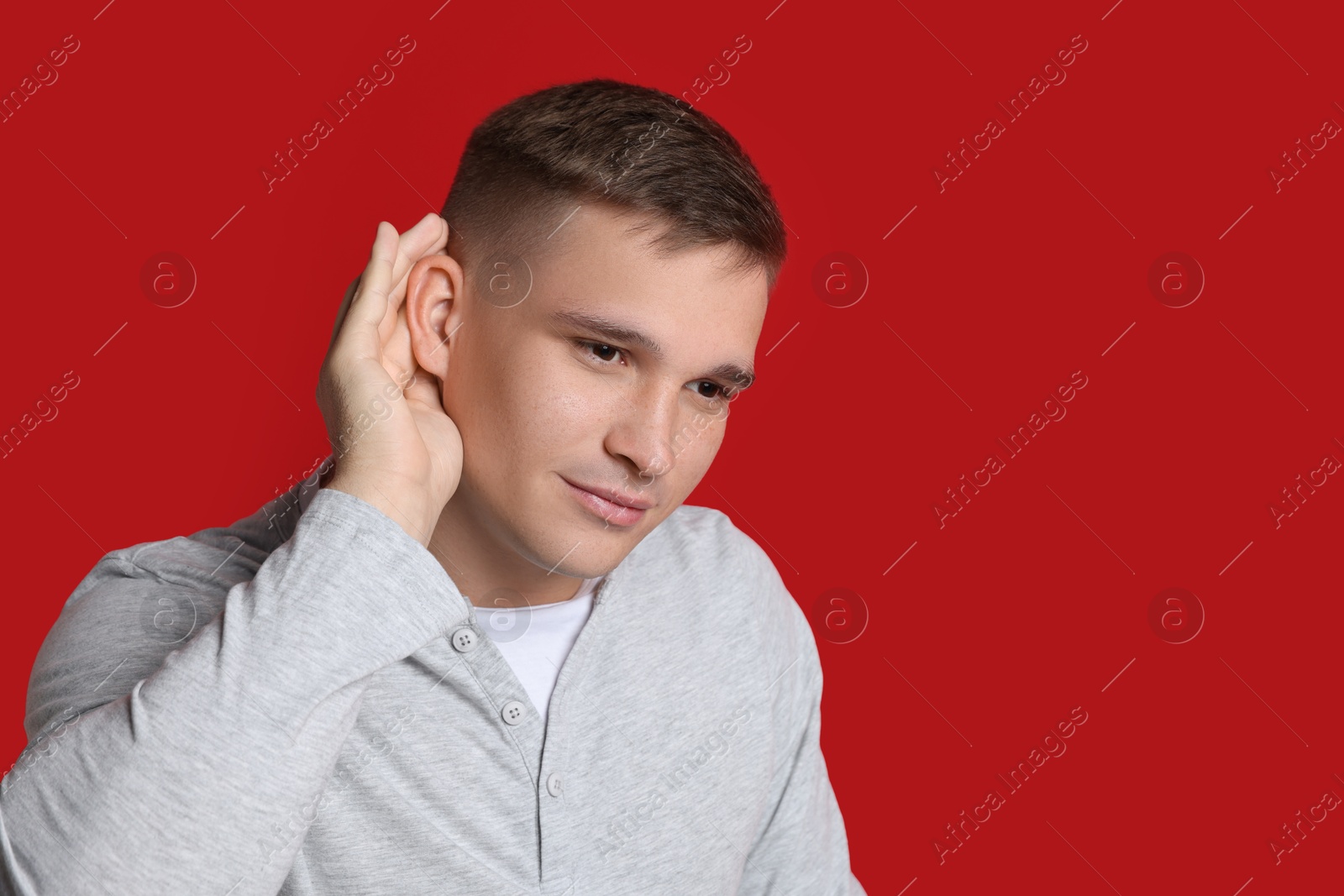 Photo of Man showing hand to ear gesture on red background, space for text