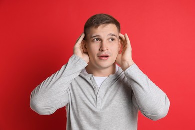 Photo of Man showing hand to ear gesture on red background