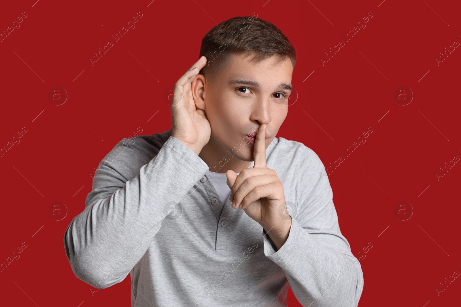 Photo of Man showing hand to ear gesture on red background