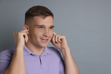 Photo of Man covering his ears with fingers on gray background, space for text