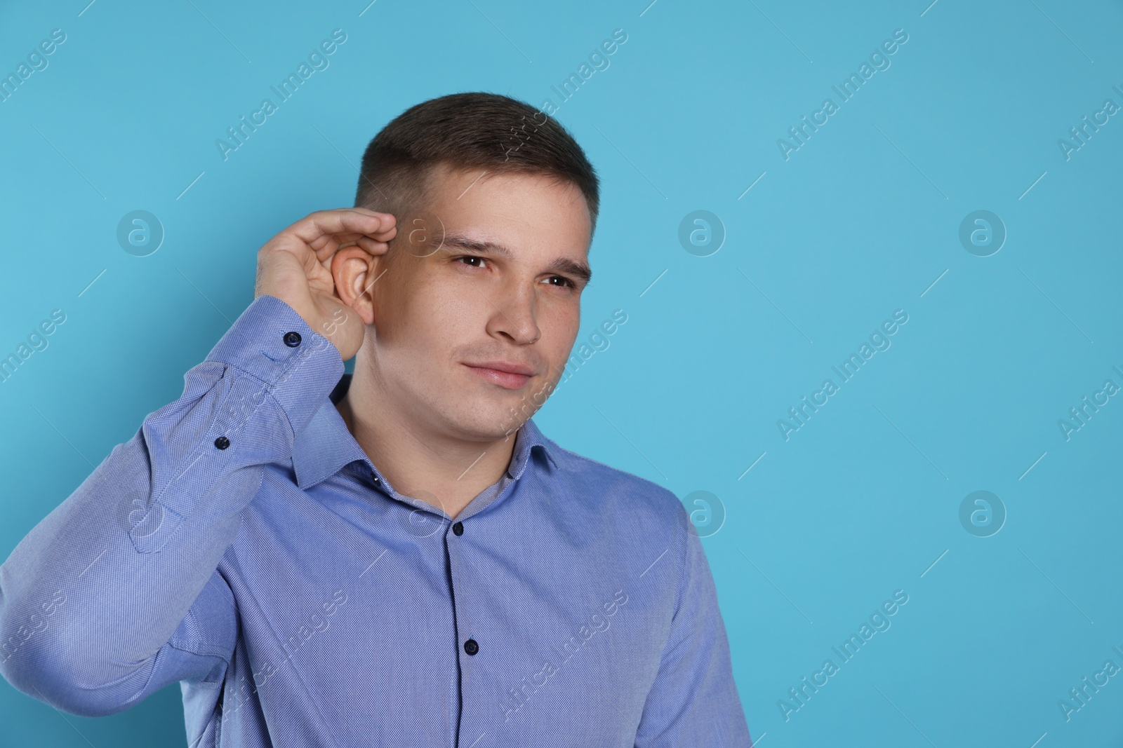 Photo of Man showing hand to ear gesture on light blue background, space for text