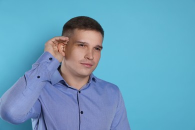 Photo of Man showing hand to ear gesture on light blue background, space for text