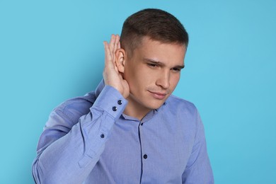 Photo of Man showing hand to ear gesture on light blue background