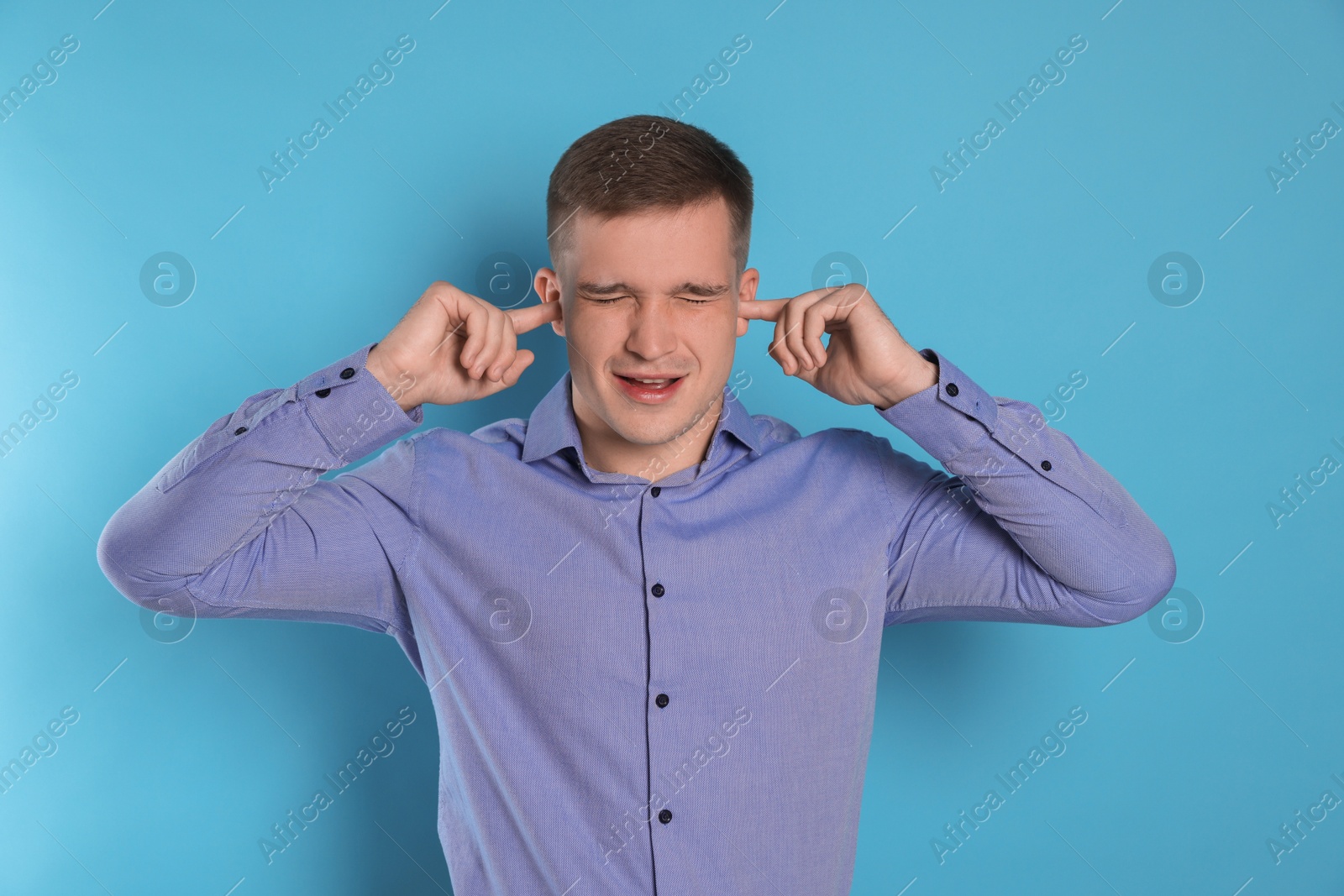 Photo of Man covering his ears with fingers on light blue background