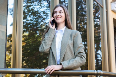 Photo of Portrait of young woman in stylish suit talking on phone outdoors