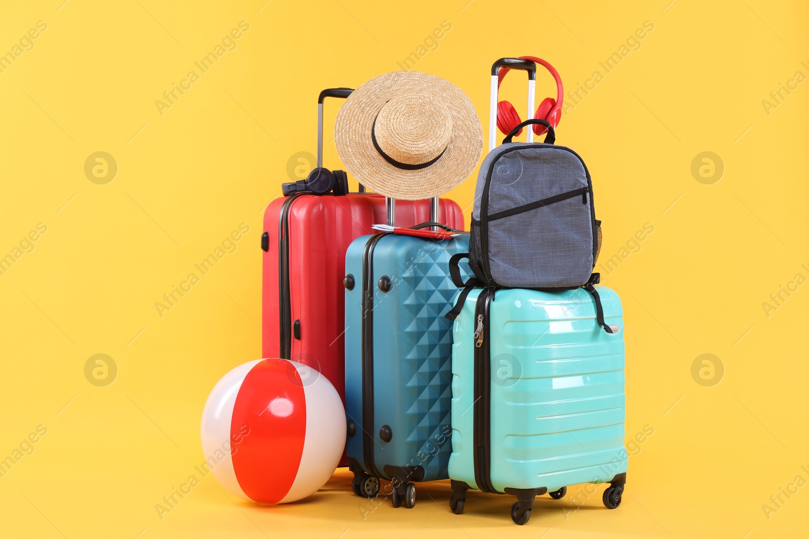 Photo of Travel abroad. Packed suitcases, backpack, beach ball and hat on yellow background