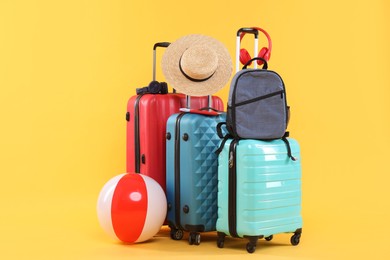 Photo of Travel abroad. Packed suitcases, backpack, beach ball and hat on yellow background