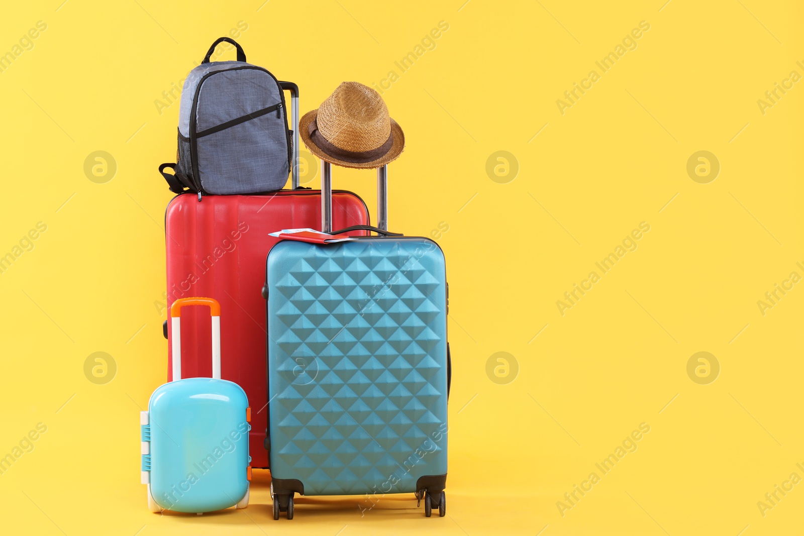 Photo of Travel abroad. Packed suitcases, backpack and hat on yellow background, space for text