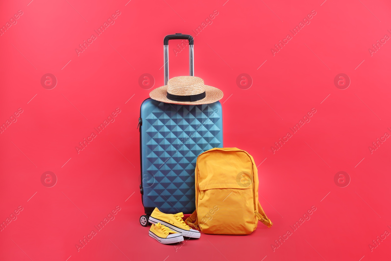 Photo of Travel abroad. Suitcase, backpack, hat and shoes on red background