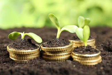 Photo of Stacks of coins with green plants on soil against blurred background, closeup. Money growth concept