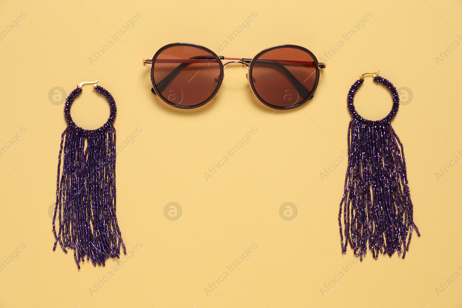 Photo of Stylish earrings and sunglasses on pale yellow background, flat lay