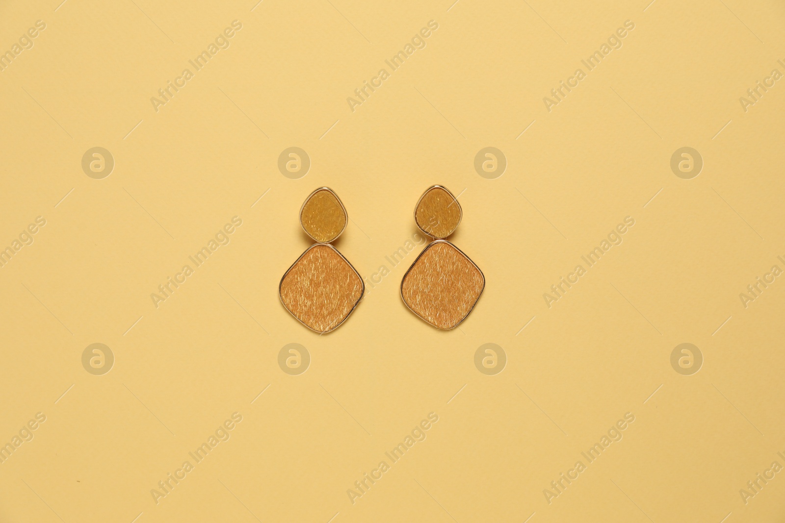 Photo of Stylish golden earrings on pale yellow background, top view