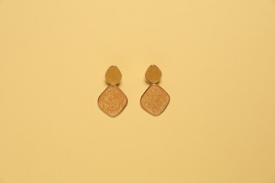 Photo of Stylish golden earrings on pale yellow background, top view