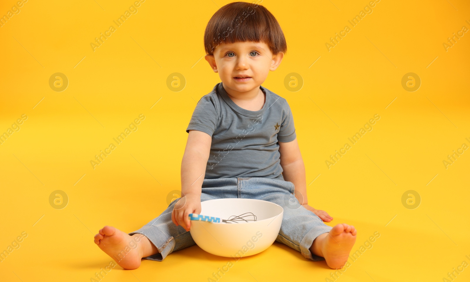 Photo of Cute little boy with bowl and whisk on yellow background