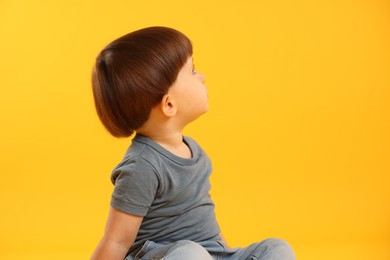 Photo of Little boy looking at something on yellow background. Space for text