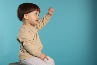 Portrait of cute little boy pointing at something on light blue background. Space for text