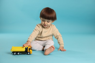 Cute little boy playing with toy truck on light blue background