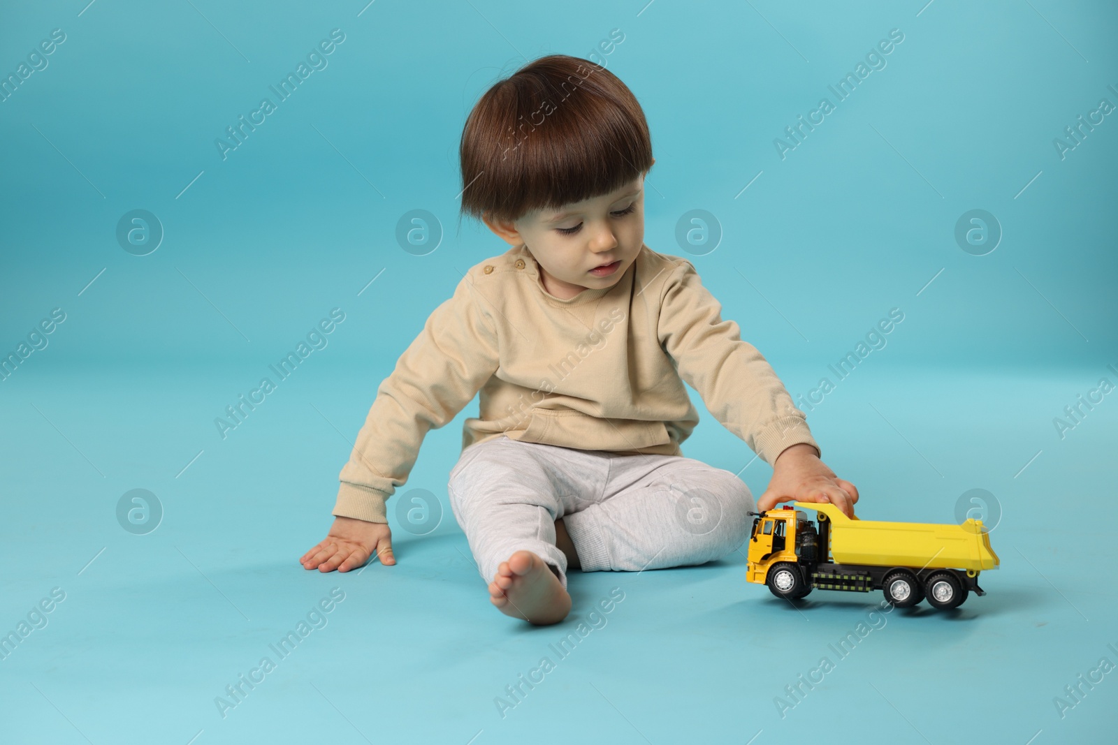 Photo of Cute little boy playing with toy truck on light blue background