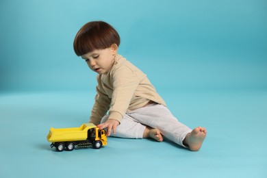 Photo of Cute little boy playing with toy truck on light blue background