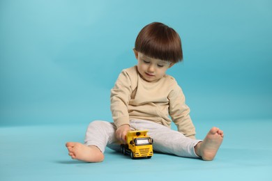 Cute little boy playing with toy truck on light blue background