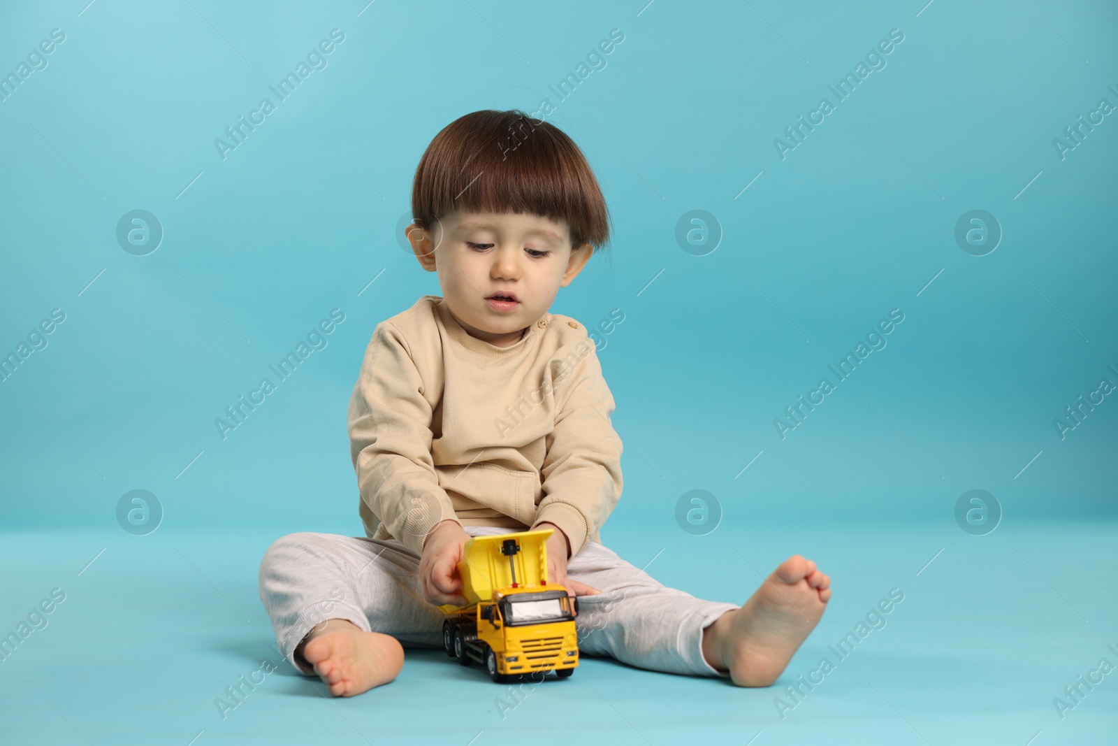 Photo of Cute little boy playing with toy truck on light blue background