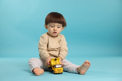 Cute little boy playing with toy truck on light blue background