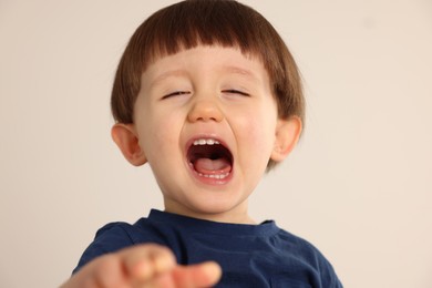 Portrait of emotional little boy on light grey background