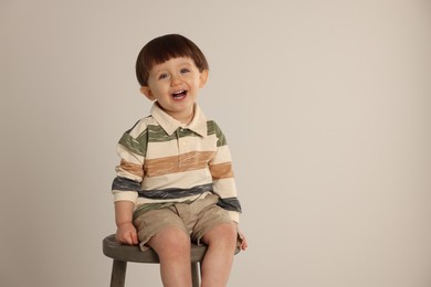 Emotional little boy sitting on stool against light grey background. Space for text