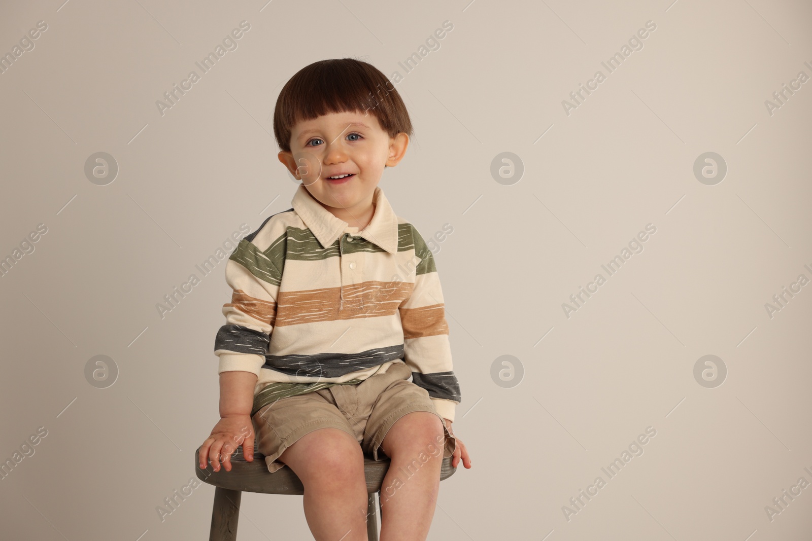 Photo of Happy little boy sitting on stool against light grey background. Space for text