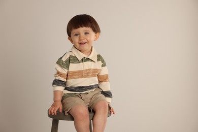 Happy little boy sitting on stool against light grey background. Space for text