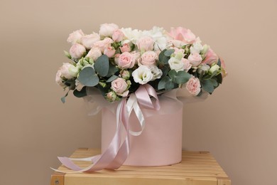 Photo of Gift box with bouquet of beautiful roses and eucalyptus branches on wooden nightstand against beige background