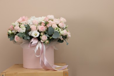 Gift box with bouquet of beautiful roses and eucalyptus branches on wooden nightstand against beige background. Space for text