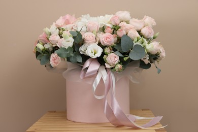 Photo of Gift box with bouquet of beautiful roses and eucalyptus branches on wooden nightstand against beige background