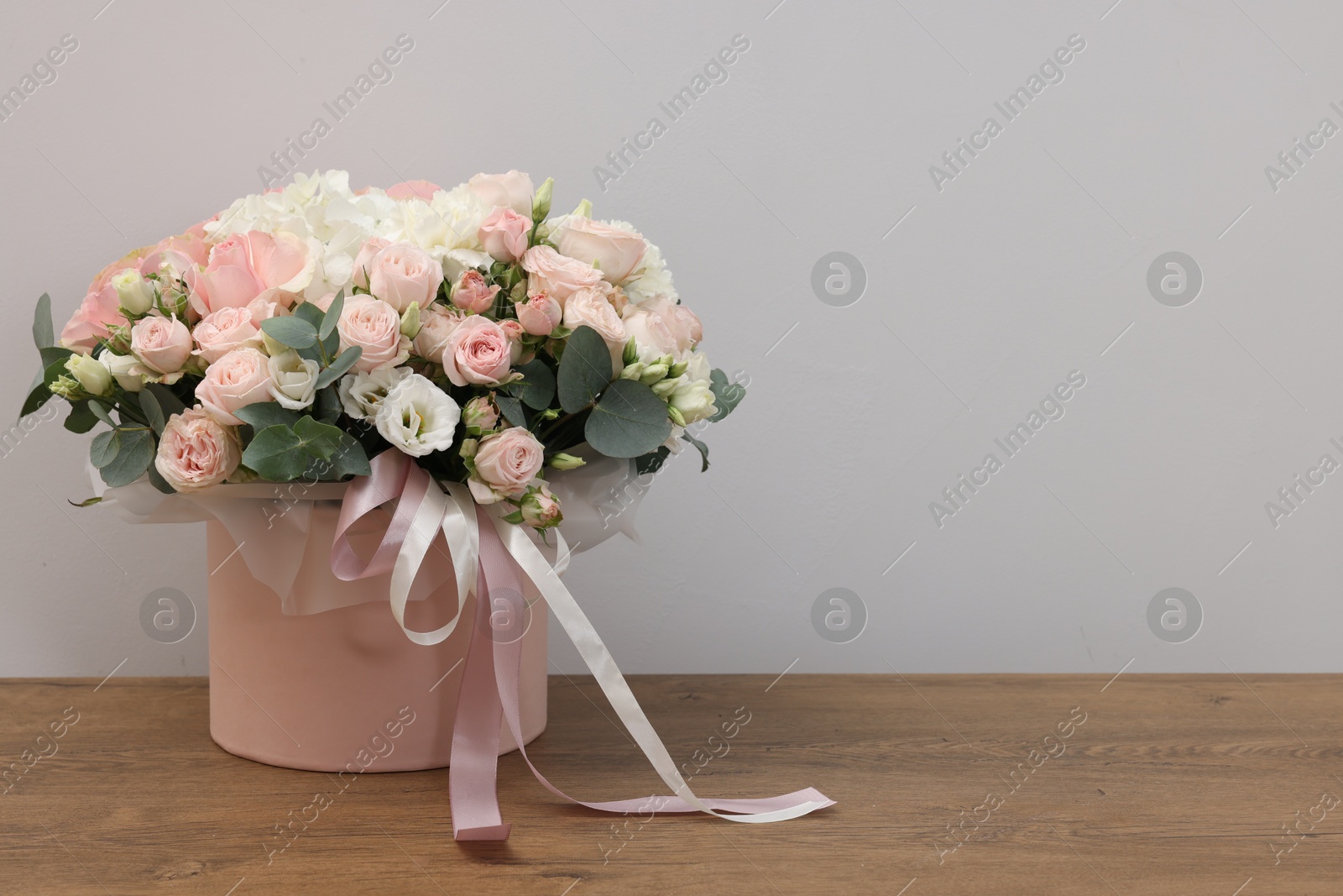 Photo of Gift box with bouquet of beautiful flowers and eucalyptus branches on wooden table against grey background. Space for text