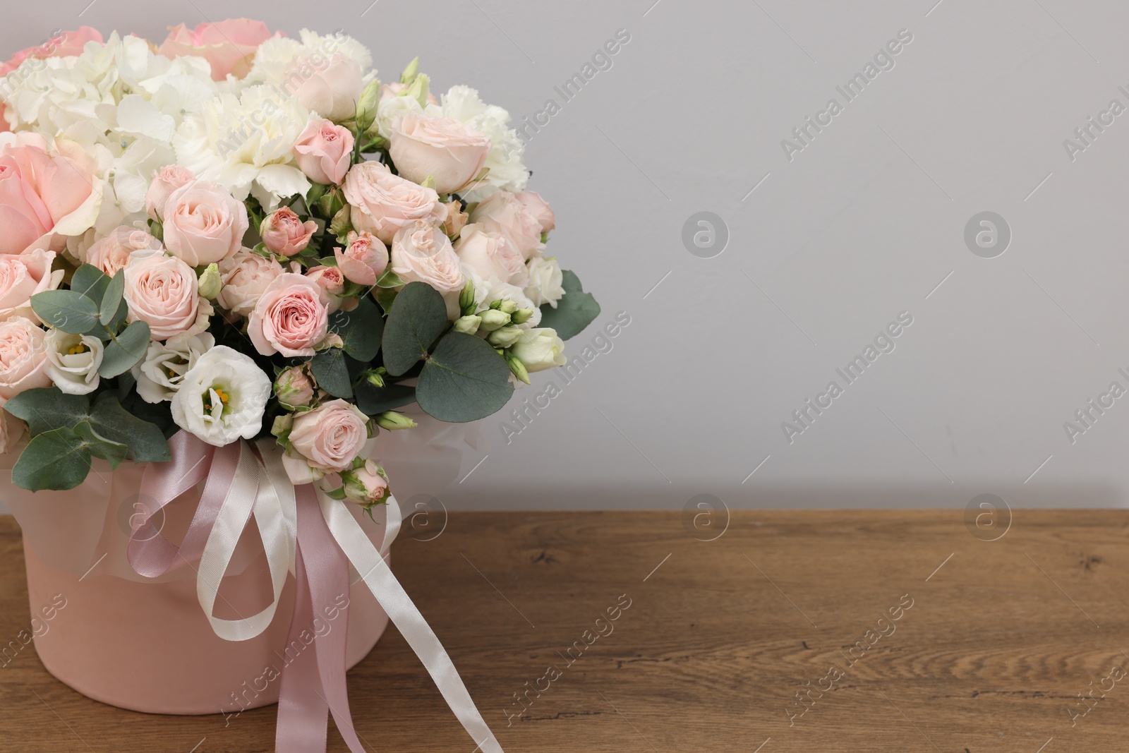 Photo of Gift box with bouquet of beautiful flowers and eucalyptus branches on wooden table against grey background, closeup. Space for text