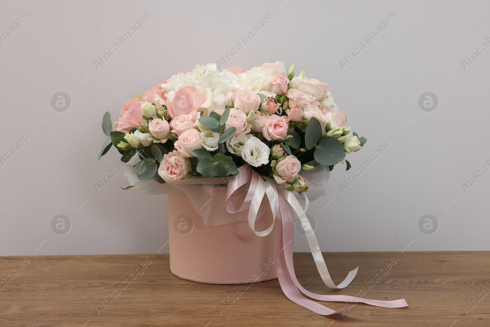 Photo of Gift box with bouquet of beautiful flowers and eucalyptus branches on wooden table against grey background