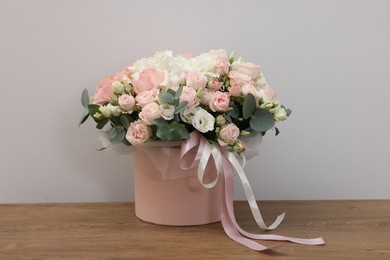 Gift box with bouquet of beautiful flowers and eucalyptus branches on wooden table against grey background