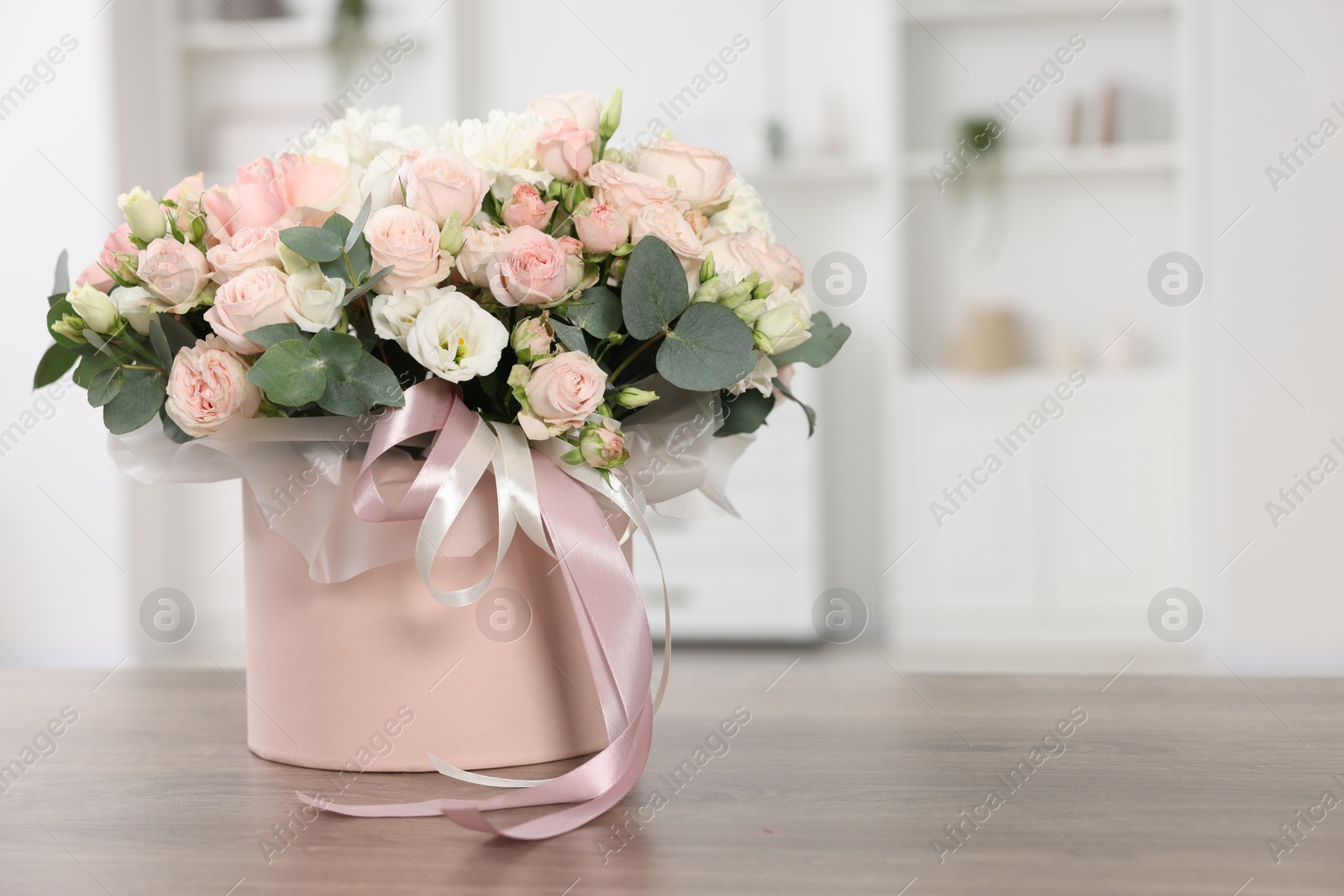 Photo of Gift box with bouquet of beautiful flowers and eucalyptus branches on wooden table against blurred background. Space for text