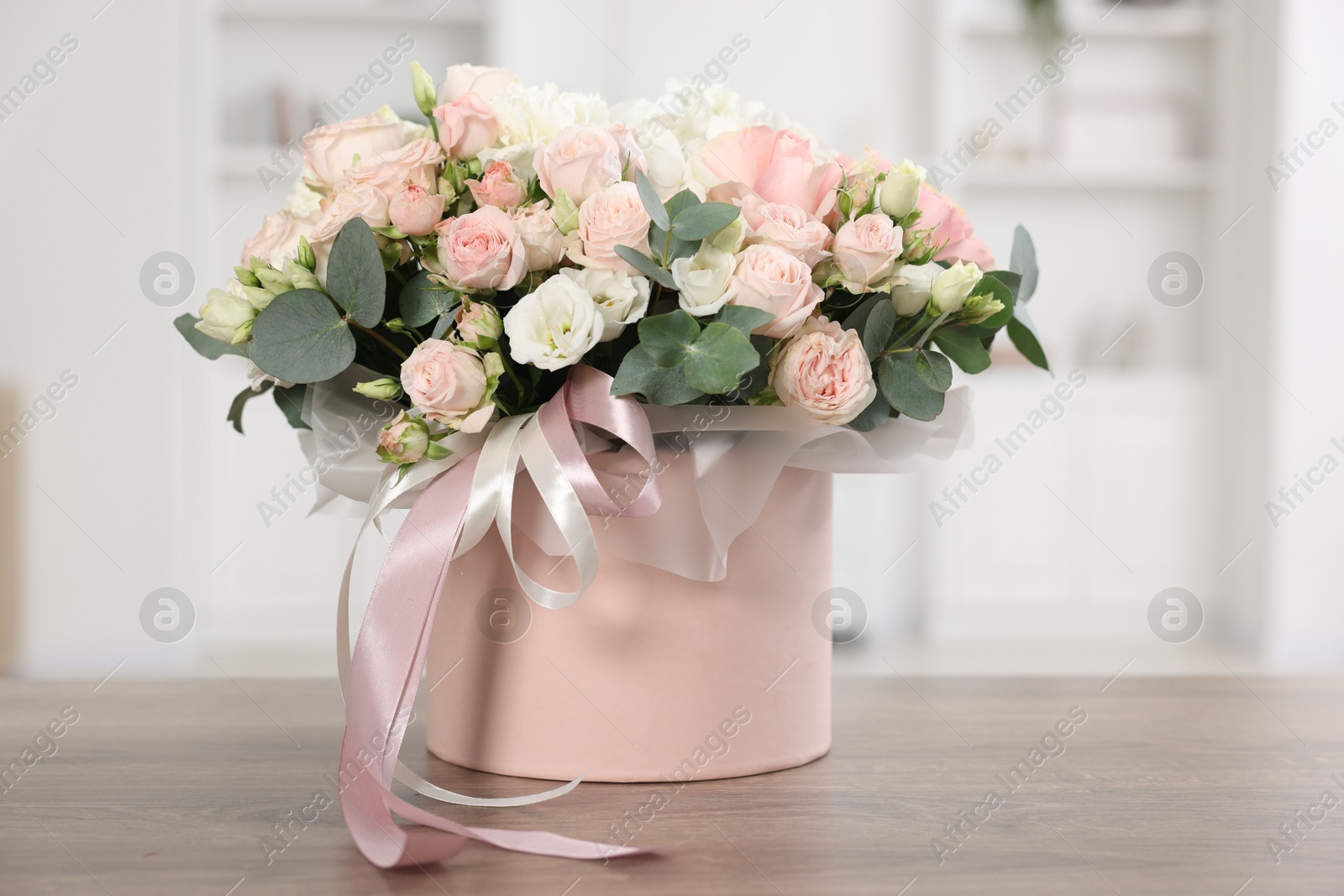 Photo of Gift box with bouquet of beautiful flowers and eucalyptus branches on wooden table against blurred background