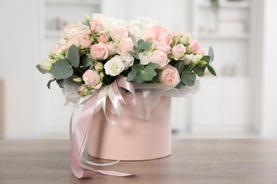 Photo of Gift box with bouquet of beautiful flowers and eucalyptus branches on wooden table against blurred background