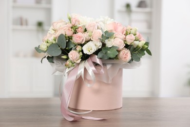 Gift box with bouquet of beautiful flowers and eucalyptus branches on wooden table against blurred background