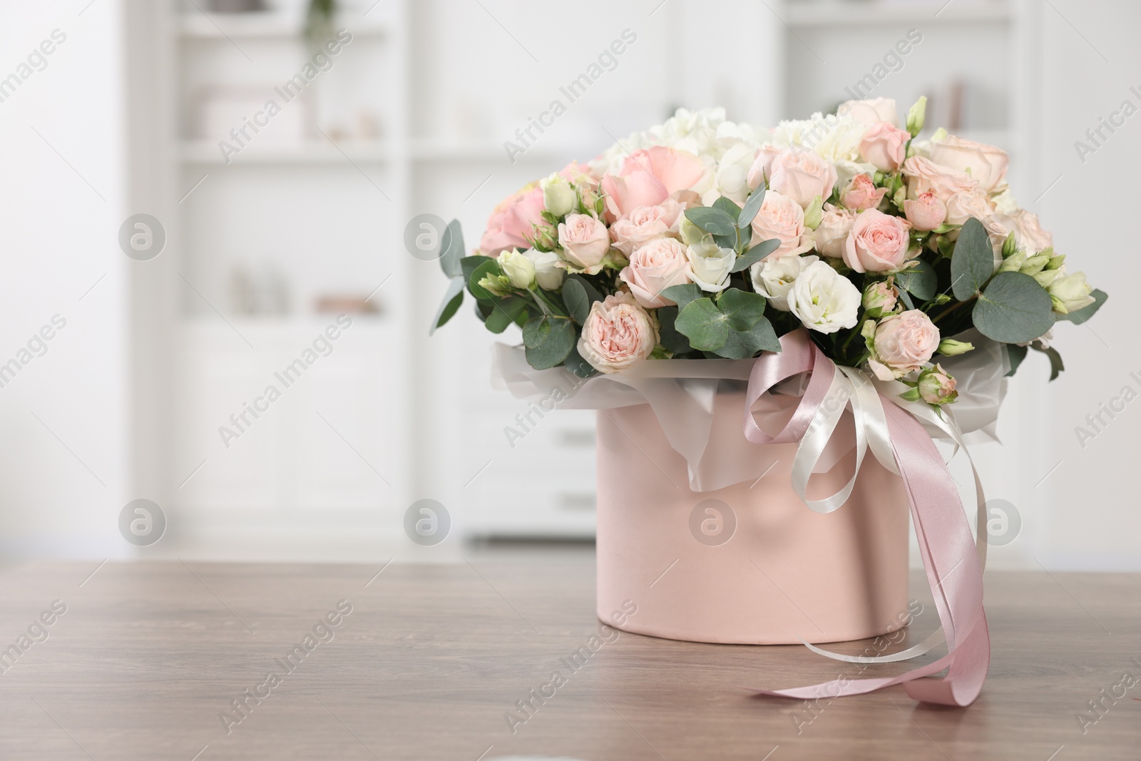 Photo of Gift box with bouquet of beautiful flowers and eucalyptus branches on wooden table against blurred background. Space for text