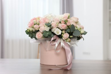 Photo of Gift box with bouquet of beautiful flowers and eucalyptus branches on wooden table against blurred background