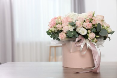 Photo of Gift box with bouquet of beautiful flowers and eucalyptus branches on wooden table against blurred background. Space for text