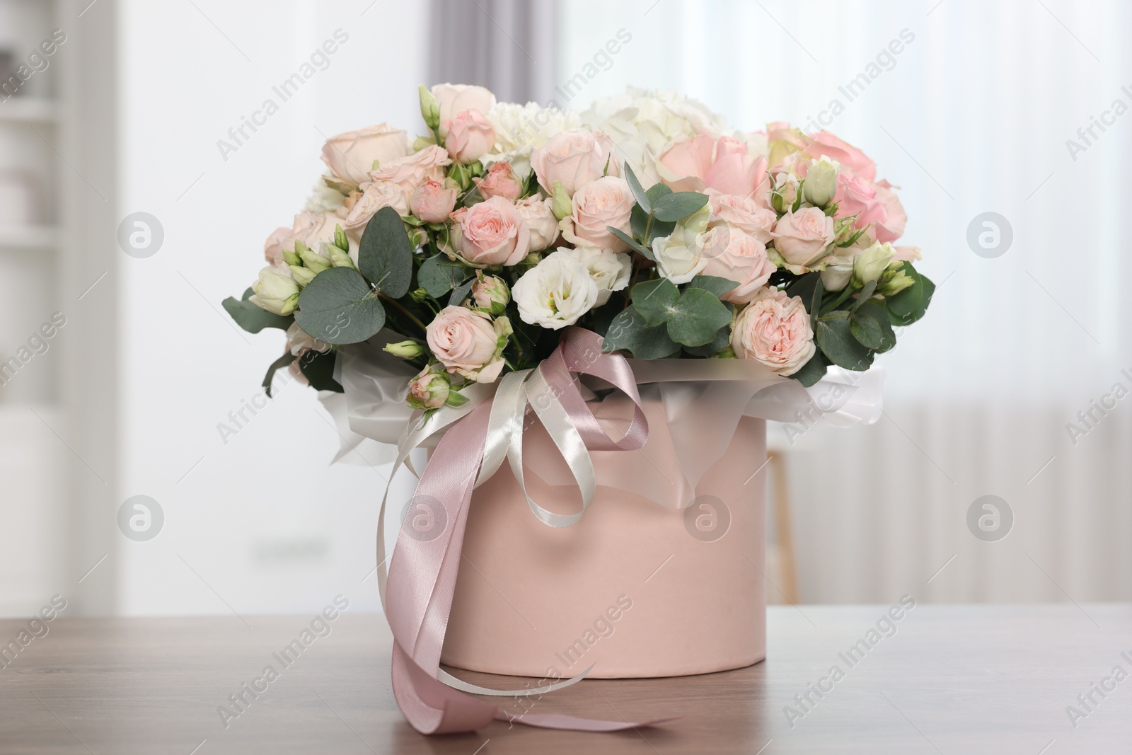 Photo of Gift box with bouquet of beautiful flowers and eucalyptus branches on wooden table against blurred background