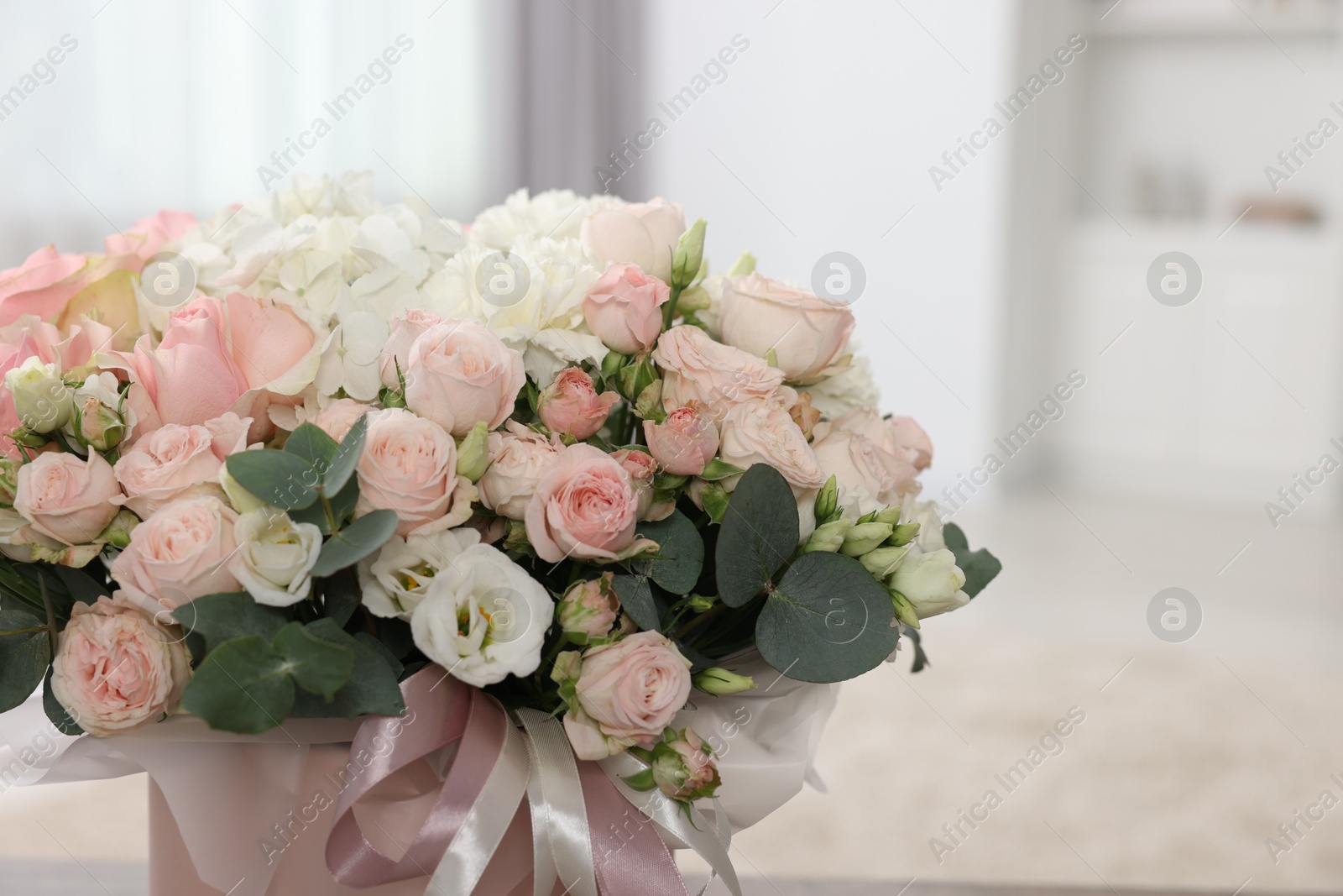 Photo of Gift box with bouquet of beautiful flowers and eucalyptus branches against blurred background, closeup