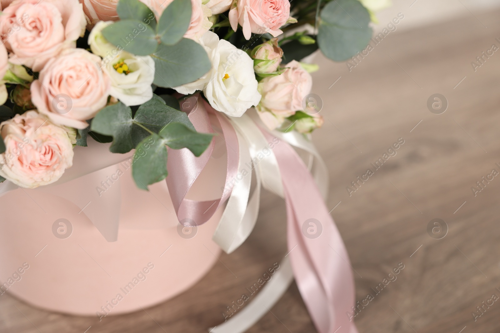 Photo of Gift box with bouquet of beautiful flowers and eucalyptus branches on wooden table, closeup. Space for text