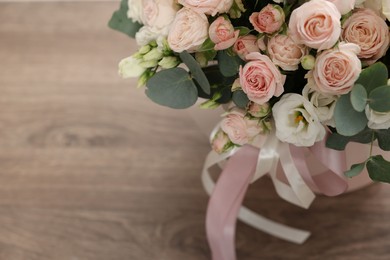 Photo of Gift box with bouquet of beautiful flowers and eucalyptus branches on wooden table, closeup. Space for text