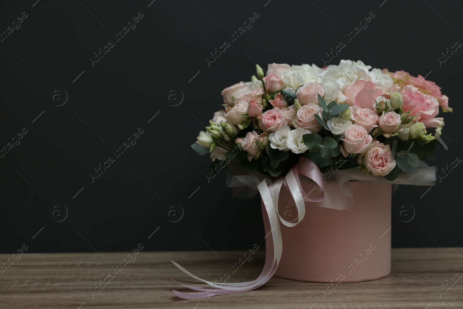 Photo of Gift box with bouquet of beautiful flowers and eucalyptus branches on wooden table against black background. Space for text